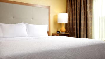 A hotel room with a large bed, a nightstand with a lamp, and a window with curtains.