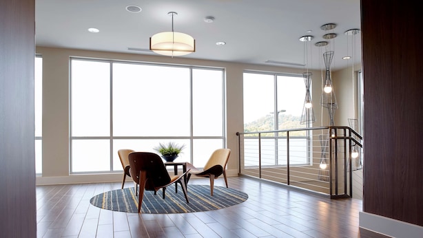 A spacious room with large windows, a wooden floor, a round rug, and a dining area with chairs. - Hampton Inn & Suites Pittsburgh Airport South–Settlers Ridge (Pittsburgh)