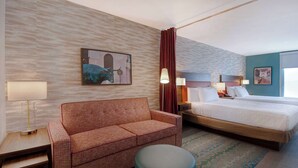 A hotel room with a bed, a sofa, a small table, and a lamp. - Home2 Suites by Hilton Waco (Waco)