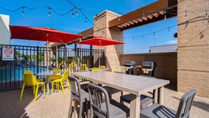 An outdoor patio with a pool, a barbecue area, and yellow chairs. - Home2 Suites by Hilton Waco (Waco)