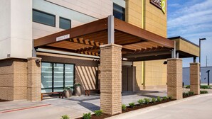 A hotel entrance with a covered waiting area, a bench, and a clear sign indicating a 10-foot clearance. - Home2 Suites by Hilton Waco (Waco)