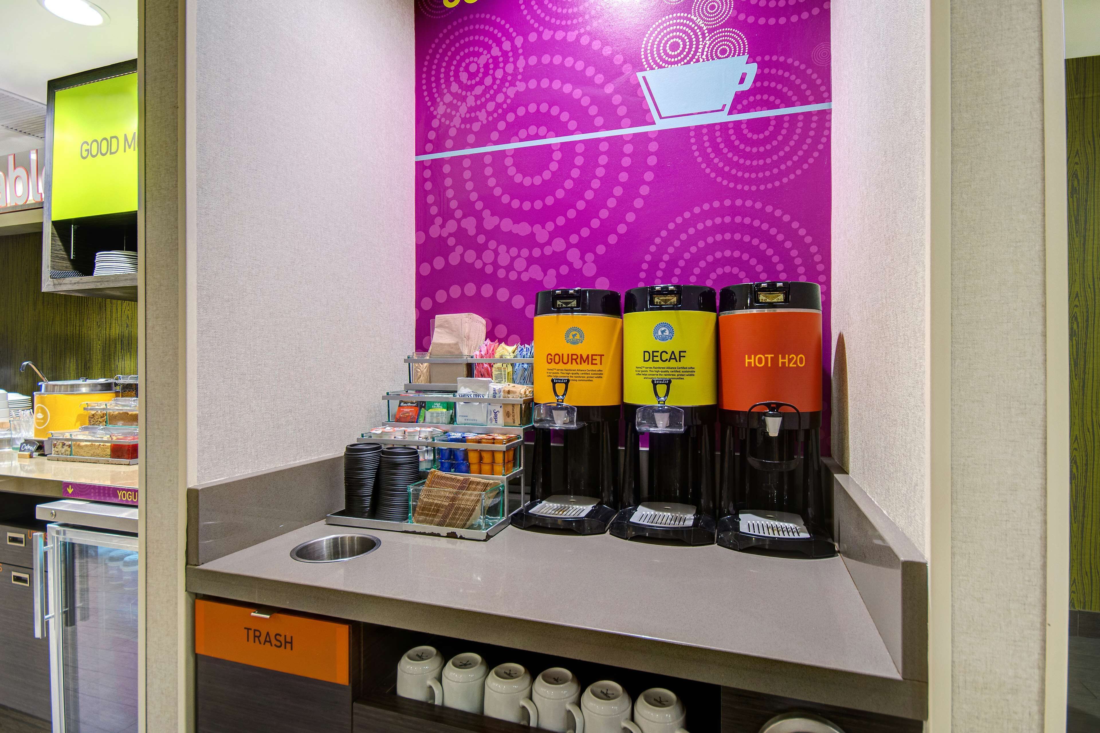 A coffee station with Gourmet, Decaf, and Hot Water options, a trash bin, and a yogurt display.