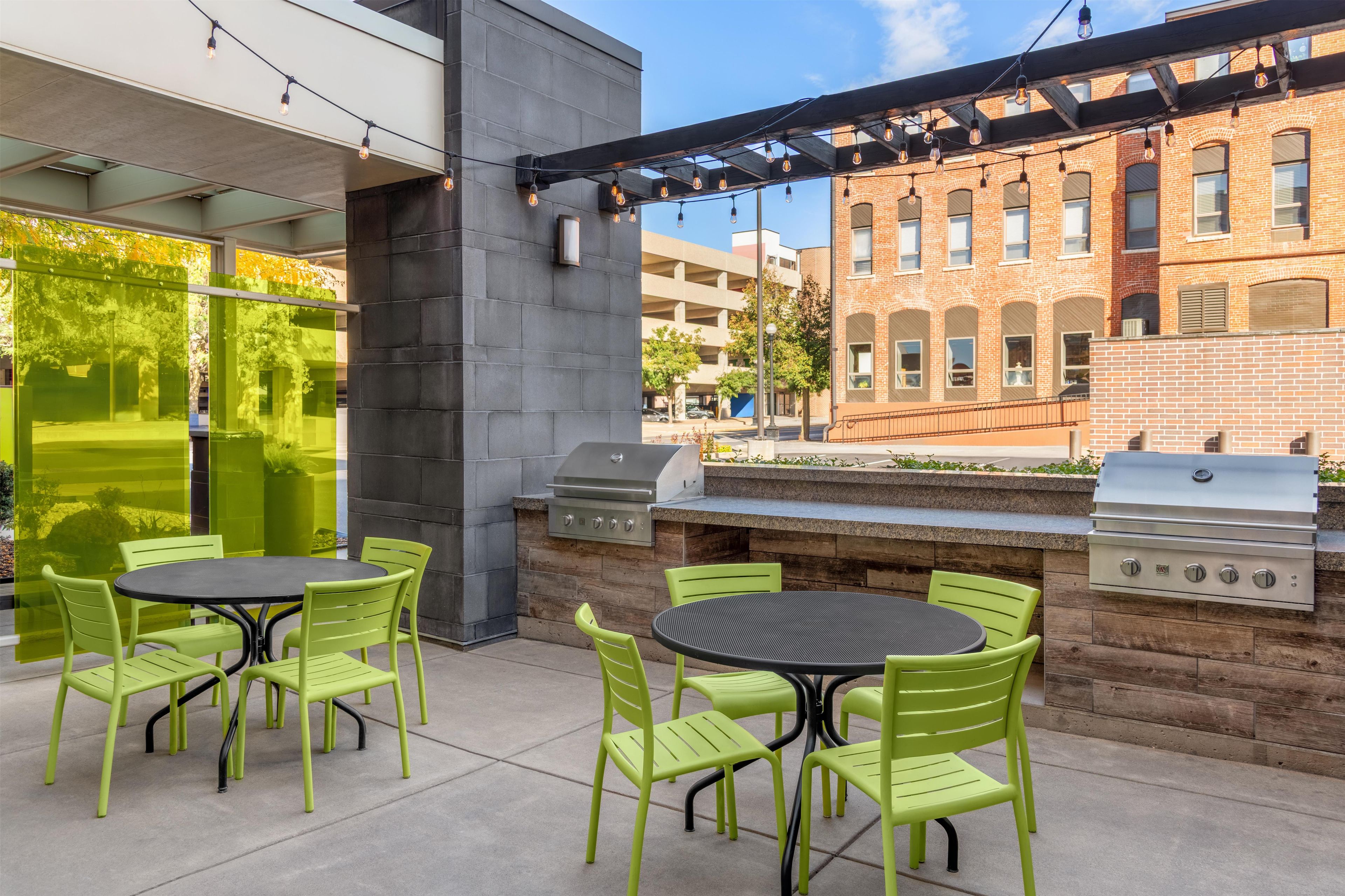 Un patio exterior con sillas verdes y una parrilla.