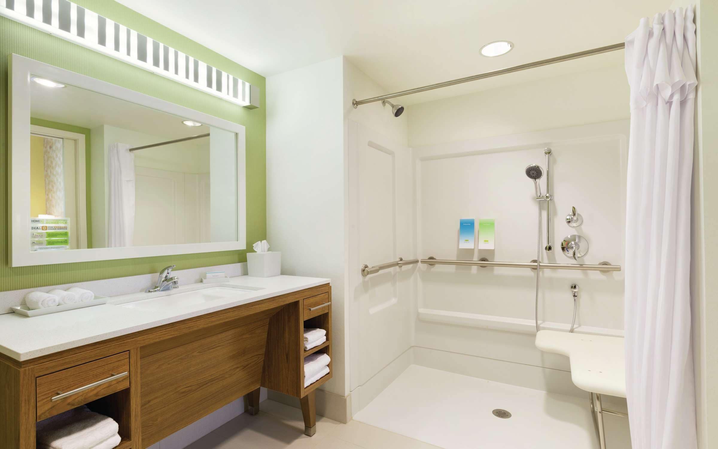 Un baño con tocador de madera, un espejo grande, ducha con puerta de cristal y un lavabo blanco.