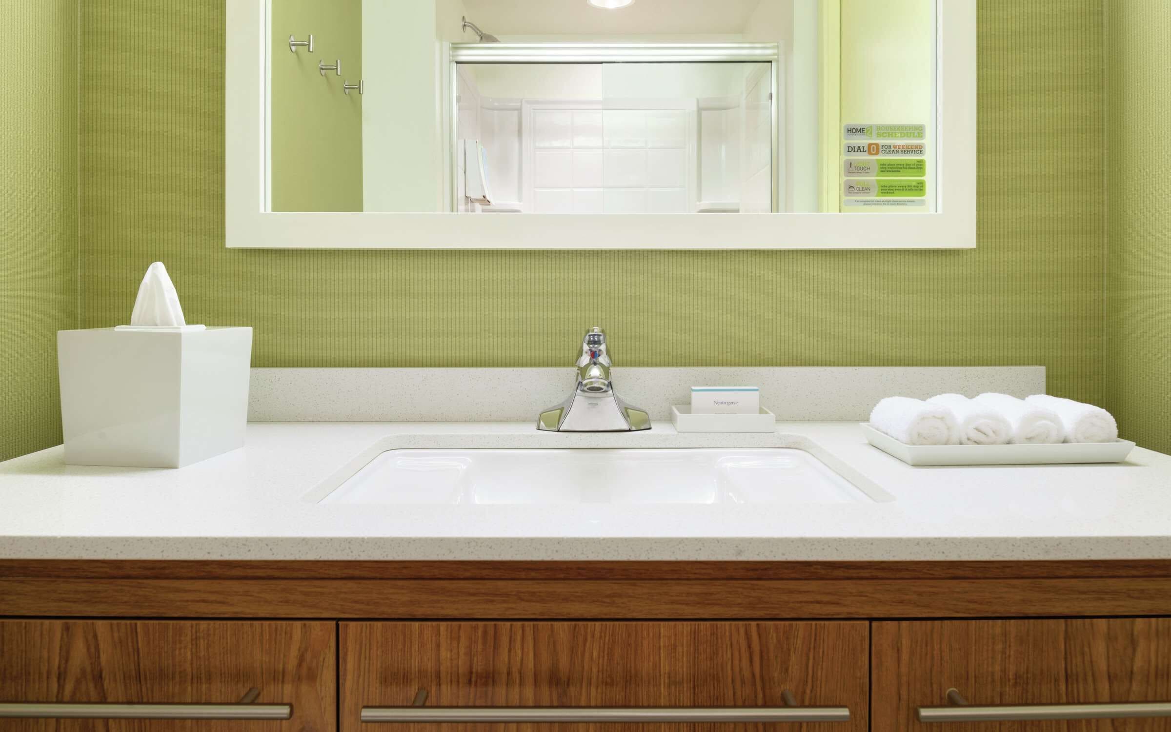 A bathroom with a white sink, a mirror, a towel rack, and a tissue box.