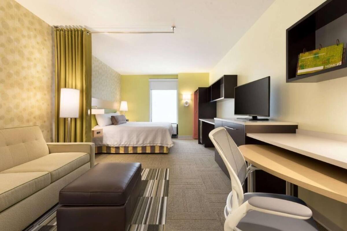 A hotel room with a bed, a sofa, a desk, a chair, a television, and a lamp.