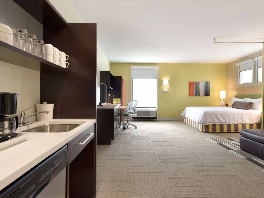 A hotel room with a kitchenette, a bed, a desk, and a chair.