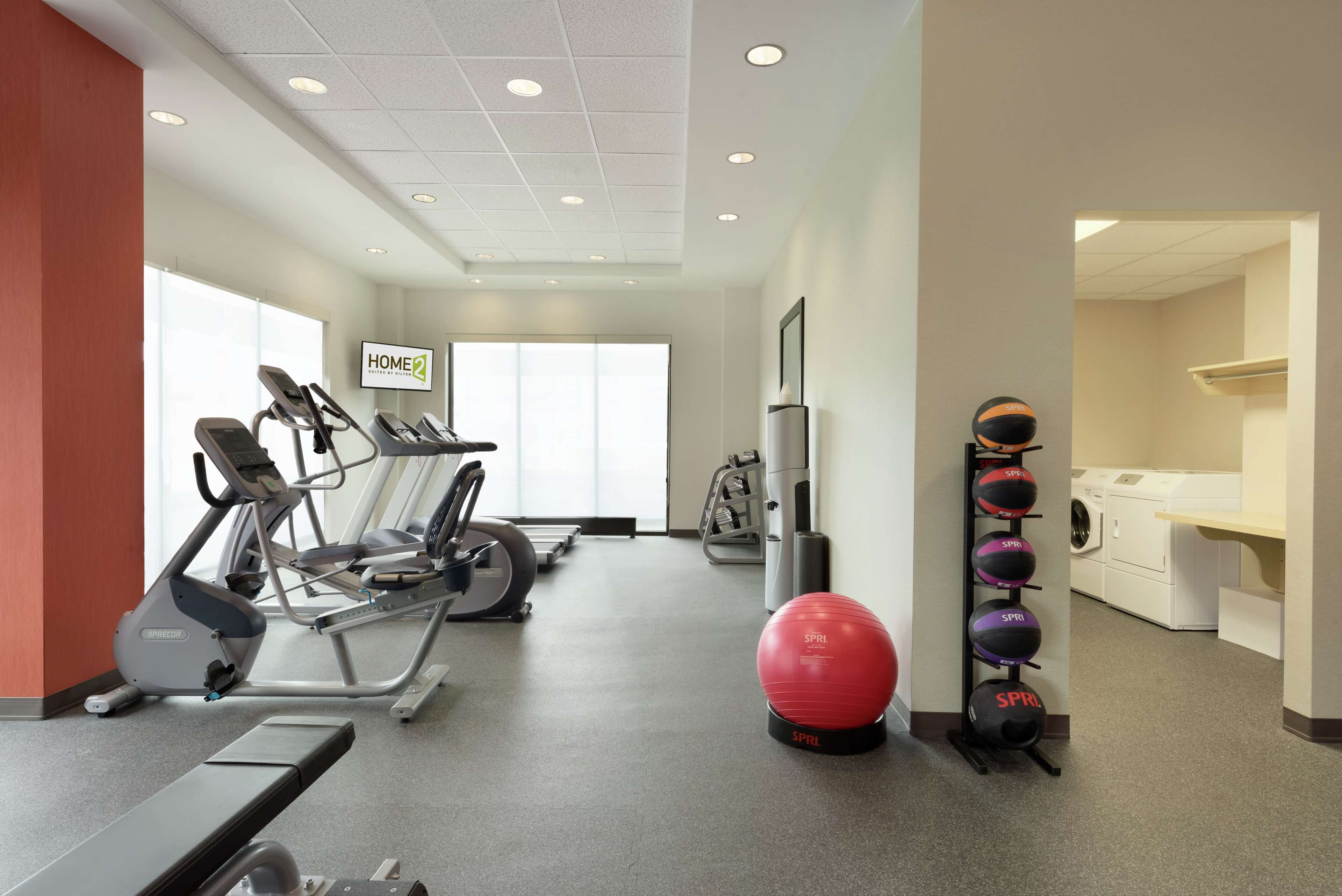 A gym with treadmills, a stationary bike, a red exercise ball, and a wall-mounted medicine ball rack.