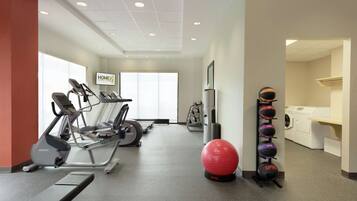 A gym with treadmills, a stationary bike, a red exercise ball, and a wall-mounted medicine ball rack.