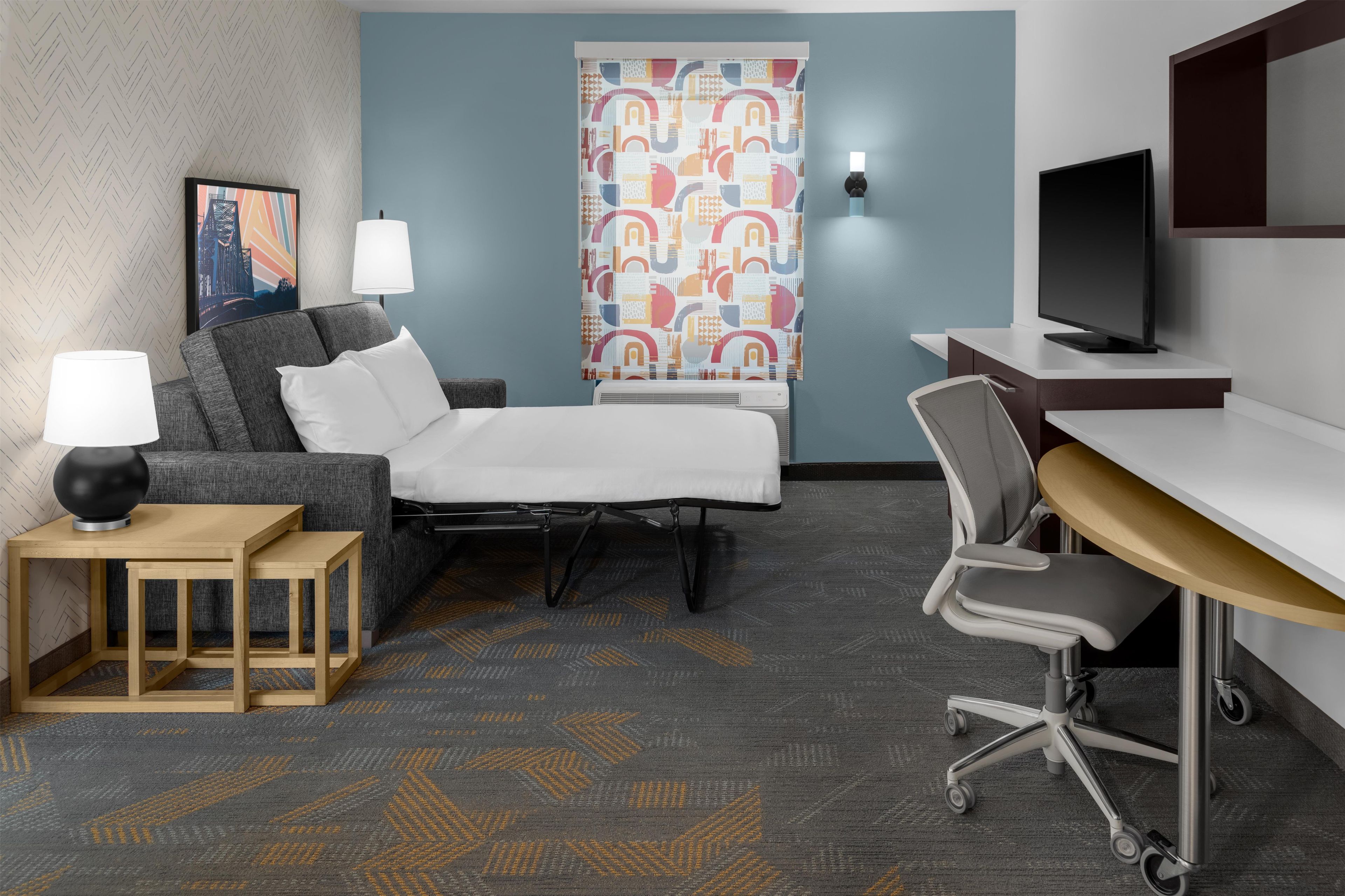 Une chambre d’hôtel équipée d’un lit, d’un bureau avec un ordinateur, d’une chaise, d’une lampe et d’un téléviseur.