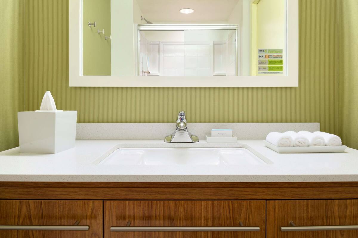 A bathroom with a white sink, a mirror, a tissue box, and a tray of towels.
