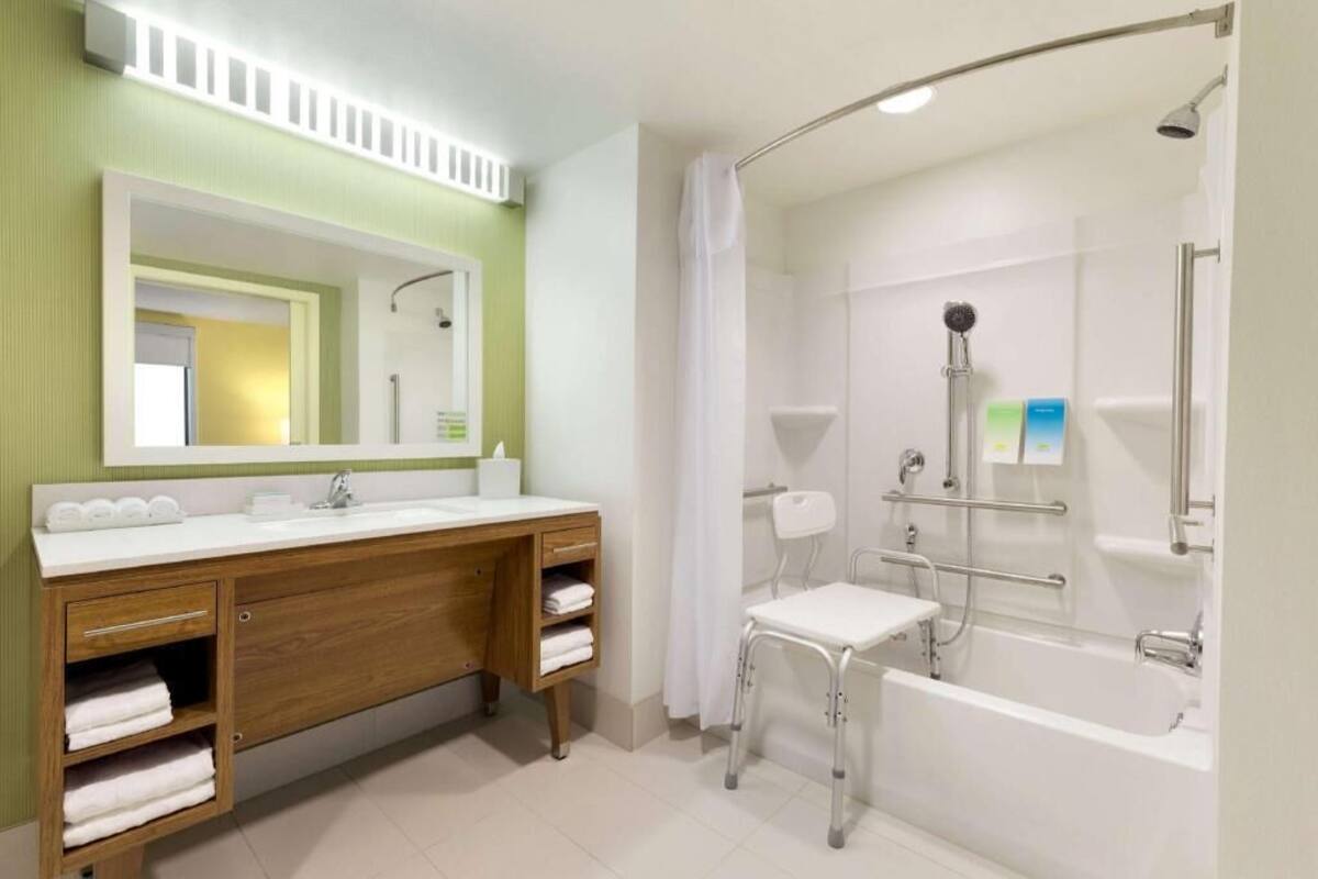 A modern bathroom with a wooden vanity, a separate sink, a shower with grab bars, and a white bathtub.