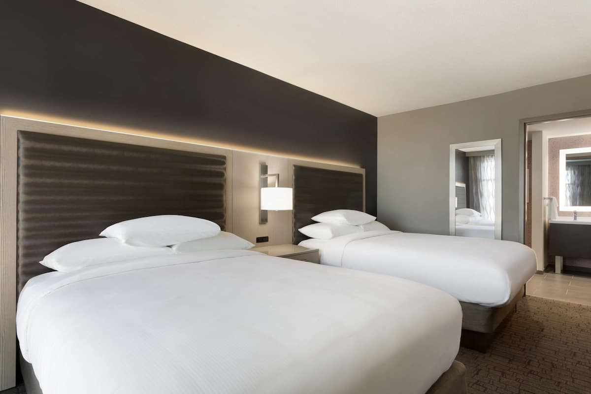 Hotelkamer met twee bedden, een nachtkastje, een lamp en een zichtbare badkamer door een geopende deur.