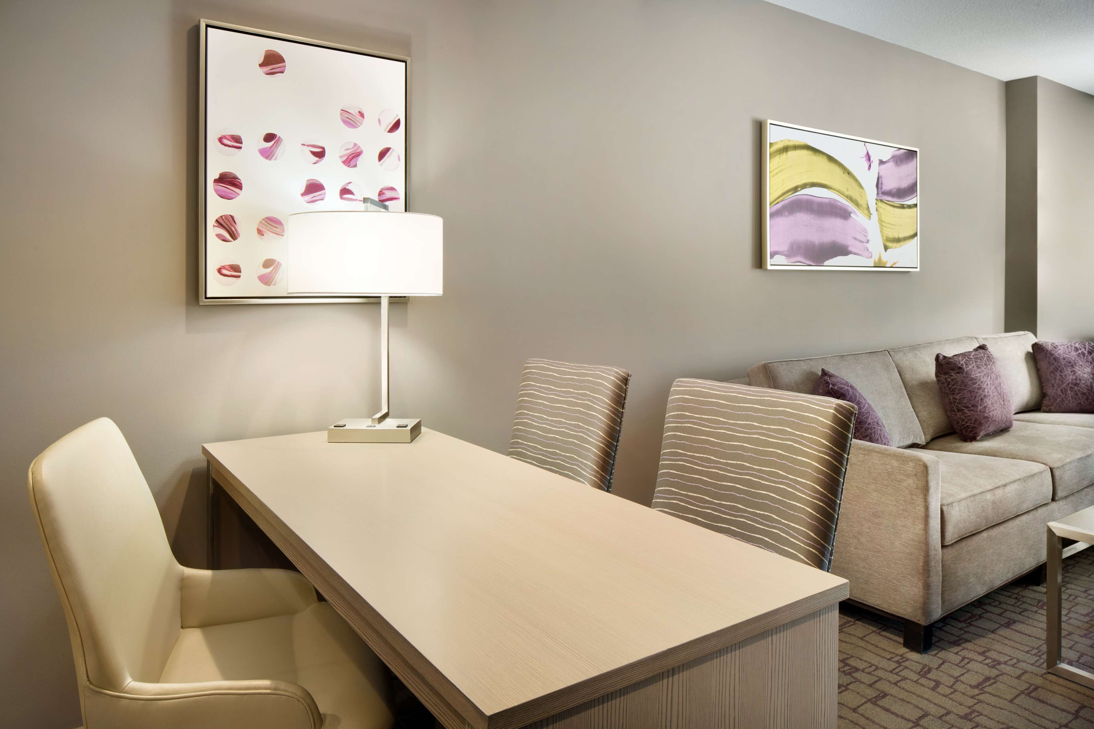 A modern hotel room with a dining table, a sofa, and two artworks on the walls.