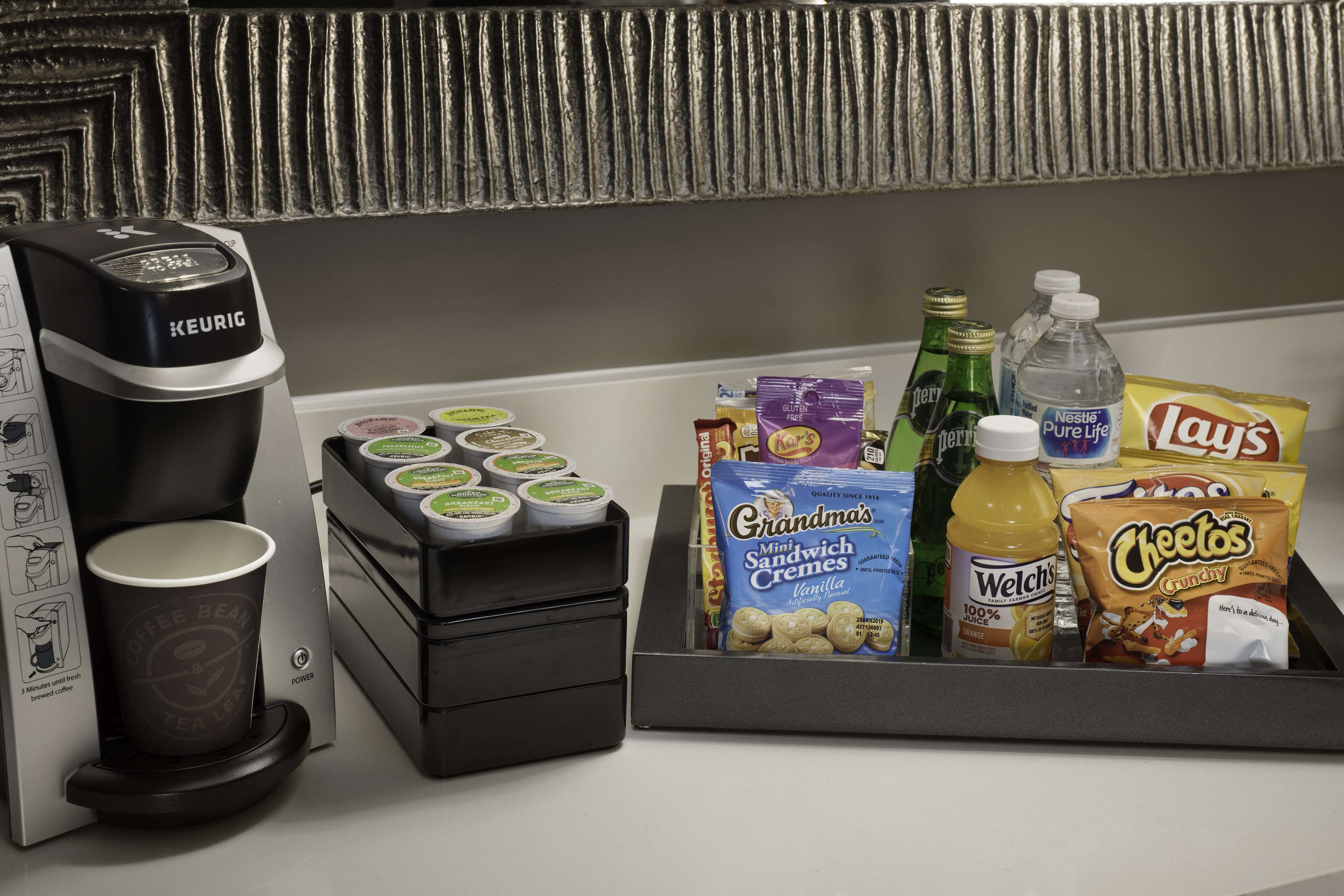 Eine Kaffeemaschine, ein Tablett mit Snacks und eine Wasserflasche auf einer Arbeitsplatte.