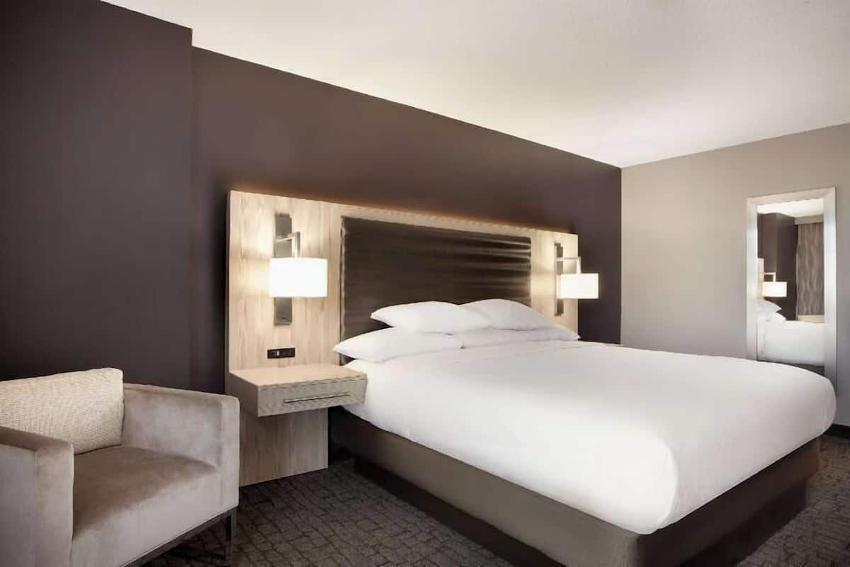 Een hotelkamer met een groot bed, een nachtkastje, een stoel en een spiegel.