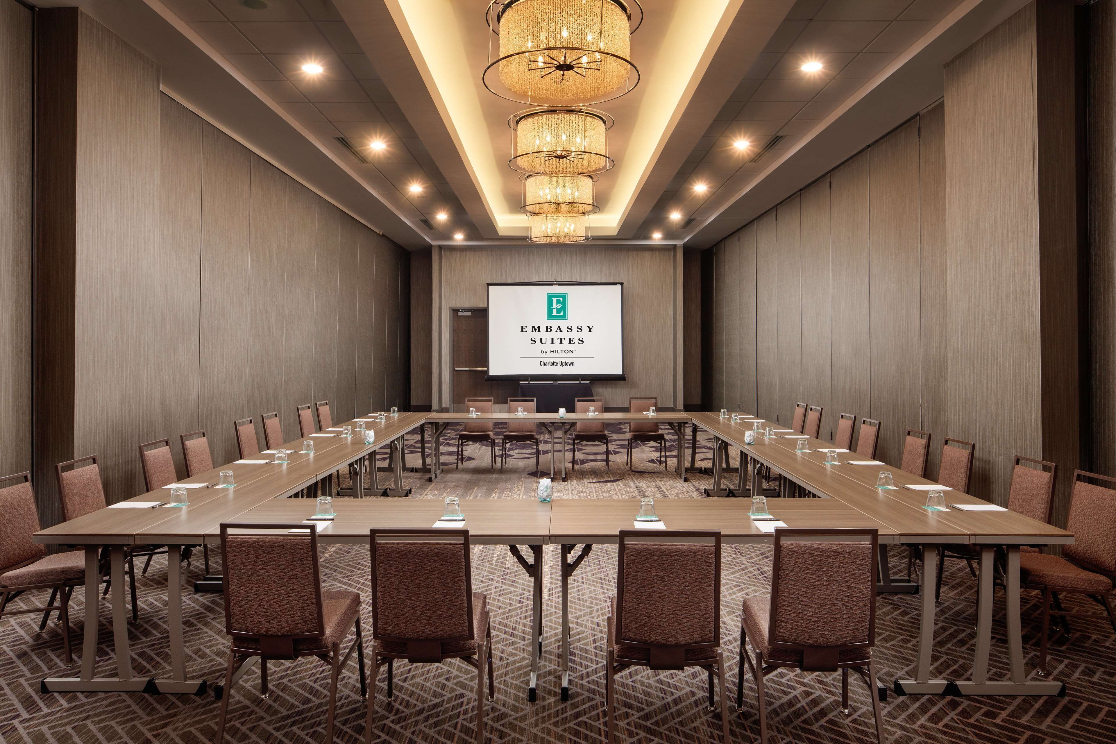 A conference room with a long table, chairs, and a screen displaying 'Embassy Suites by Hilton'.