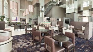 Een ruime hotellobby met een modern design, met een centraal zitgedeelte met banken en stoelen, een bar en een trap naar de bovenverdiepingen.
