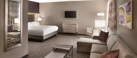A hotel room with a bed, a sofa, a desk, a TV, and a mirror.