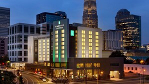 Een hotel met een opvallend 'Embassy Suites' bord, omgeven door moderne hoogbouw en een verlichte stadsstraat in de schemering.