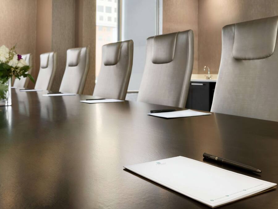 A conference room with a long table, several chairs, a vase with flowers, and a pen on the table.