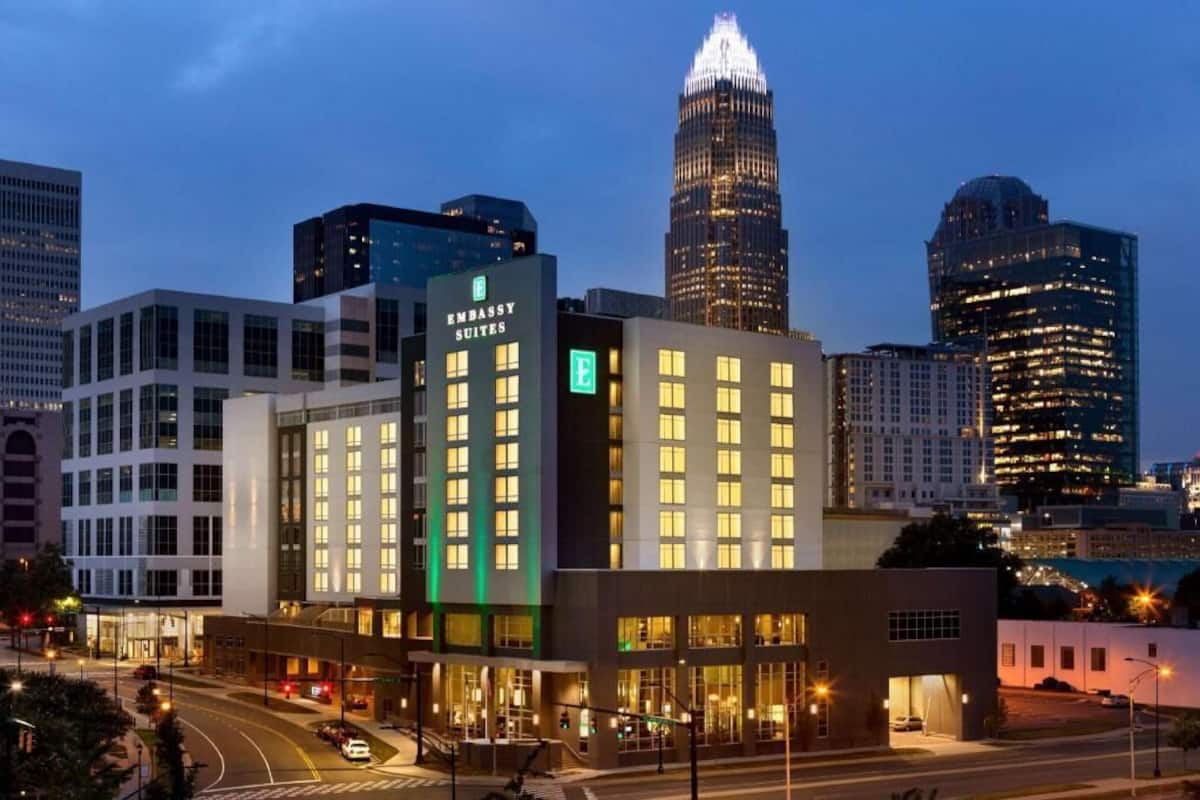 Een hotel met een modern design, een opvallend 'Embassy Suites' bord en een uitzicht op de skyline in de schemering.