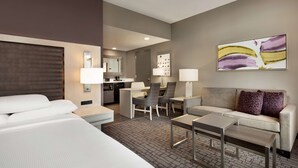 Een hotelkamer met een bed, een slaapbank, een klein tafeltje, een bureau en een stoel. Er is een spiegel, een lamp en een schilderij aan de muur.