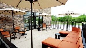 Un espace extérieur aménagé avec des murs en pierre, des chaises orange et noires, et de grands parasols.