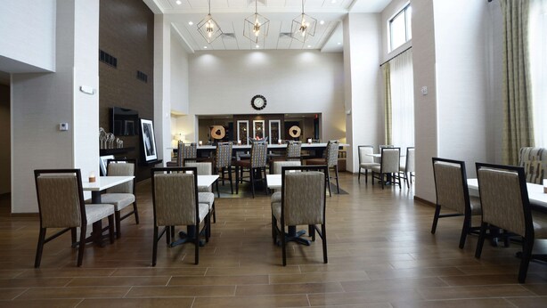 Un grand espace dédié à la salle à manger, avec plusieurs tables et chaises, une horloge au mur et des luminaires suspendus.