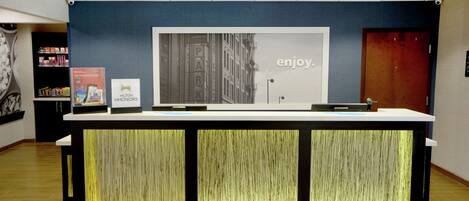 Ein Empfangsschalter mit einem großen Schild mit der Aufschrift 'enjoy', einem gerahmten Bild eines Gebäudes und einer 'Hilton Honors'-Auszeichnung.