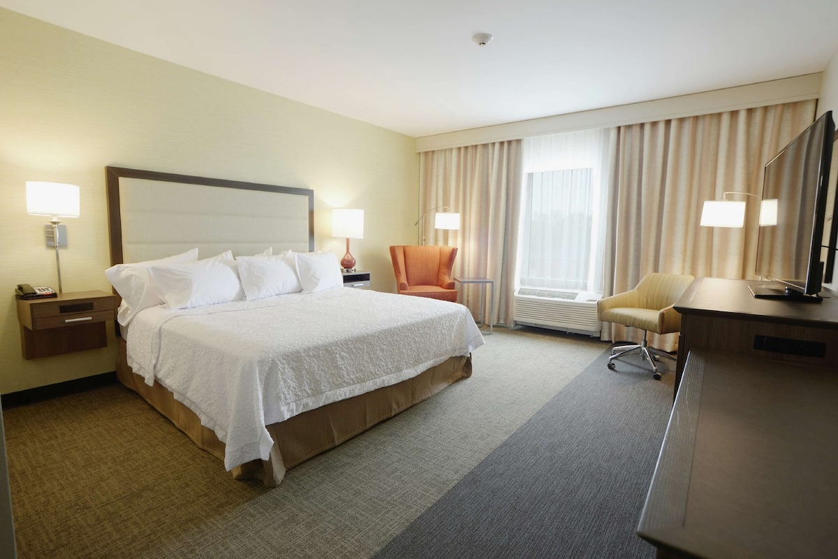 A hotel room with a bed, a desk, a chair, a television, and a window with curtains.