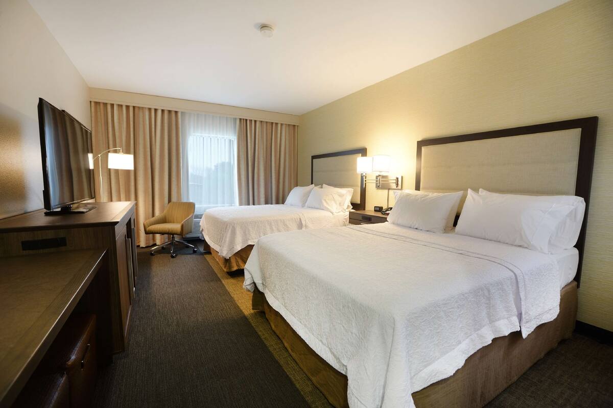A hotel room with two beds, a desk, a TV, and a lamp.