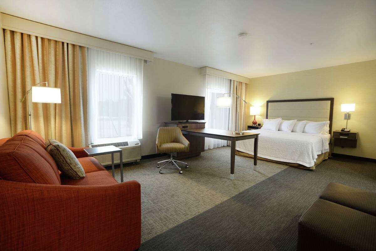 A hotel room with a bed, a desk, a TV, a chair, and a sofa.