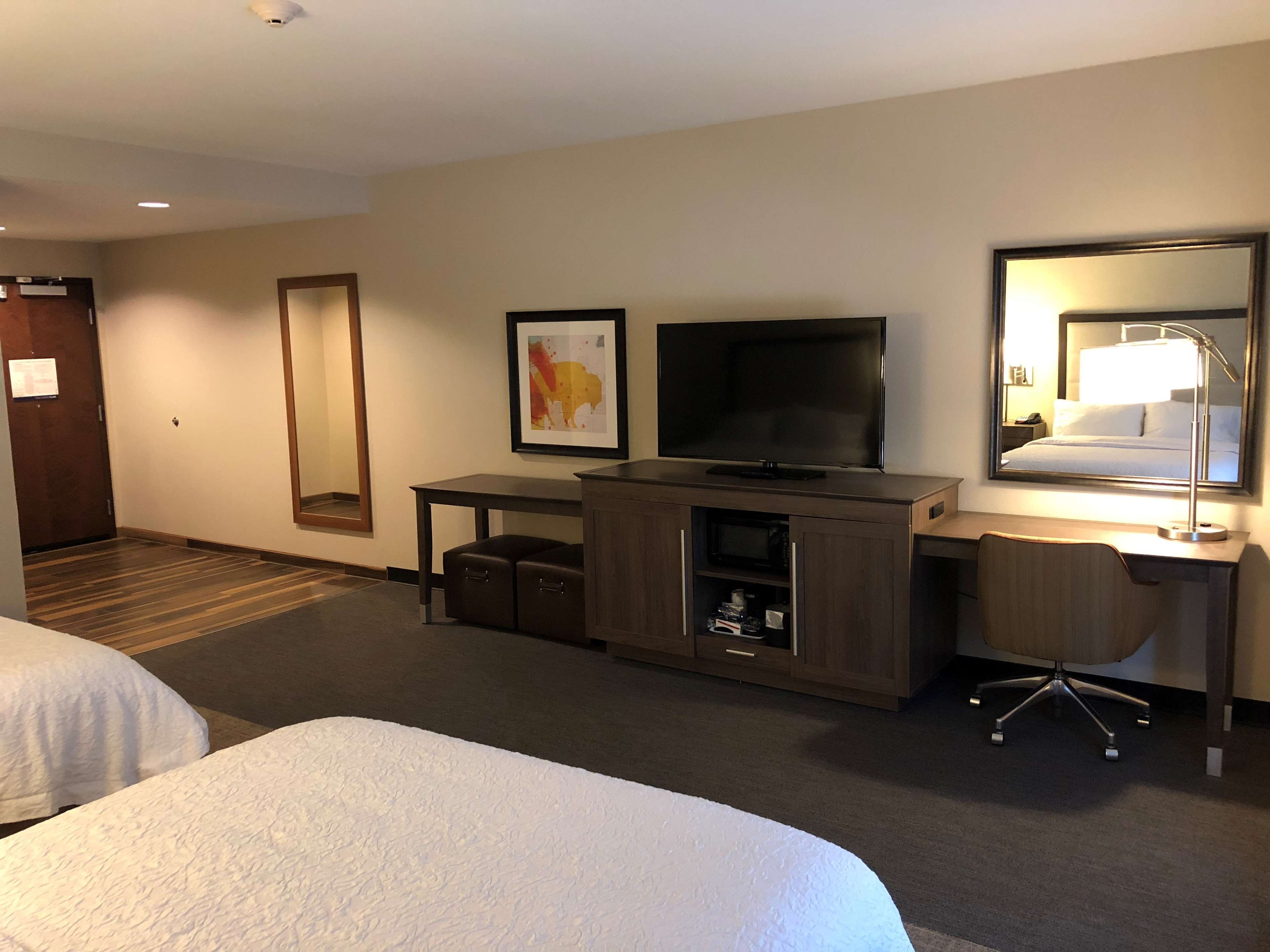 A hotel room with two beds, a desk with a computer, a television, a mirror, and a small cabinet.