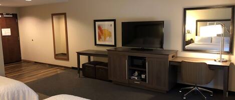 A hotel room with two beds, a desk with a computer, a television, a mirror, and a small cabinet.