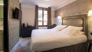 A hotel room with a bed, a television, a desk, a chair, a window with curtains, and a patterned wall.