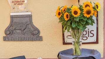 Une table dressée avec des verres à vin et un vase rempli de tournesols, une plaque décorative représentant un mouton et une enseigne avec la lettre « H ».