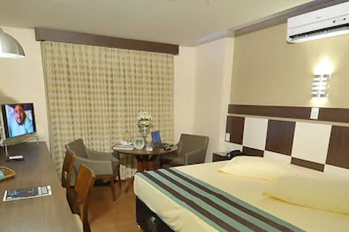 Een hotelkamer met een bed, een bureau met televisie, een stoel, een klein tafeltje en een airconditioning.