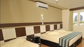 Una habitación de hotel con dos camas, una ventana con cortinas, un equipo de aire acondicionado y una lámpara fijada a la pared.