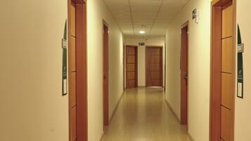Un pasillo de hotel con puertas de madera, placas de habitaciones numeradas y suelo de baldosas.