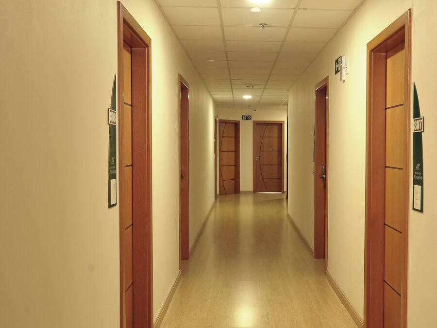 Un pasillo de hotel con puertas de madera, placas de habitaciones numeradas y suelo de baldosas.