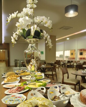 Une table de buffet garnie de divers plats, un vase décoratif orné d’une orchidée, et un coin repas avec des chaises et des tables.