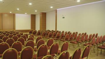 Une salle de conférence avec des rangées de chaises rouges et une scène.