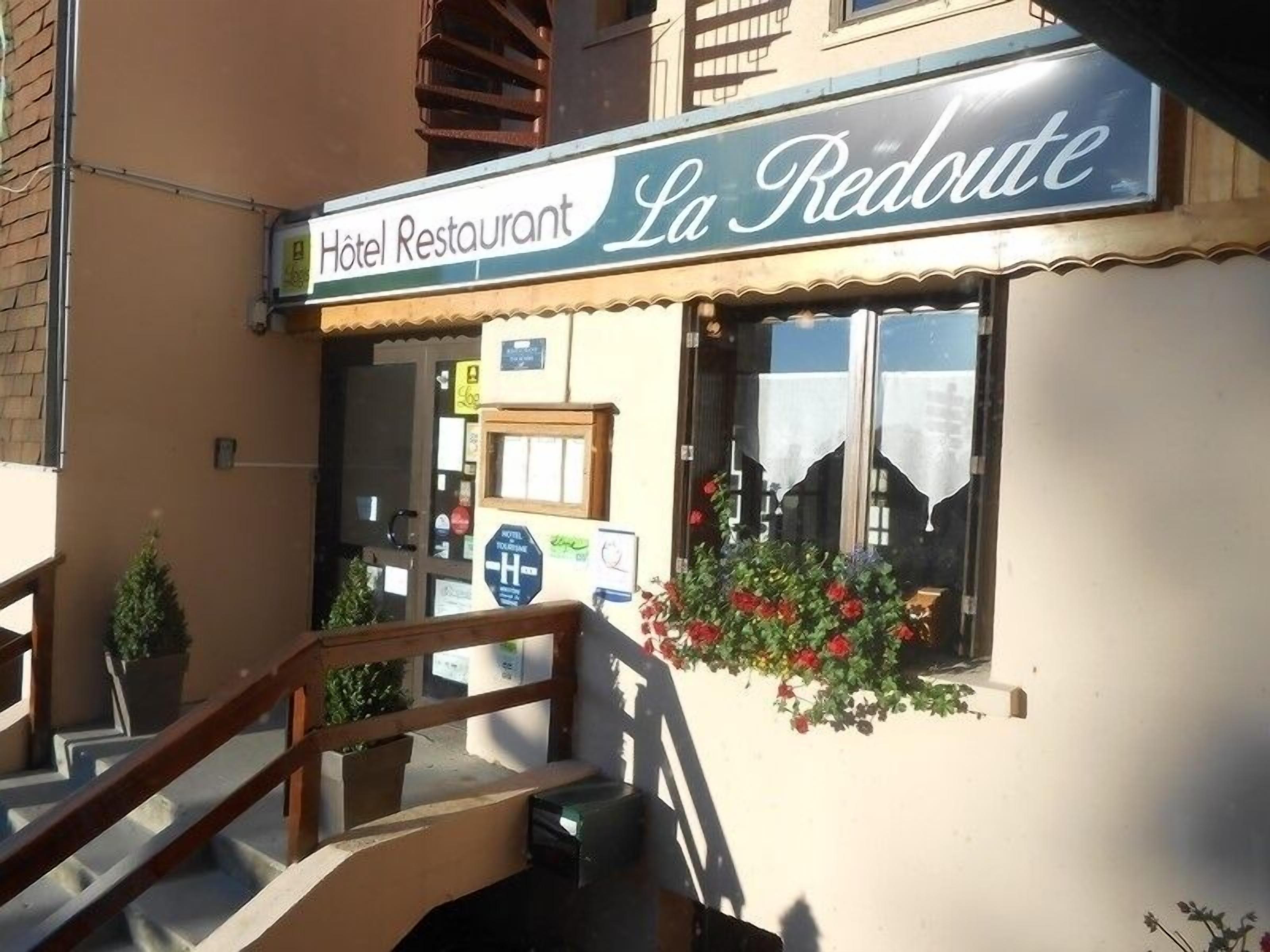 A hotel restaurant named "La Redoute" with a sign above the entrance, a staircase leading up, and a window with red flowers.