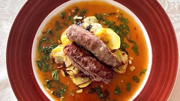 Un plato de comida con borde rojo, que contiene trozos de carne y papas en un caldo, adornado con hierbas.
