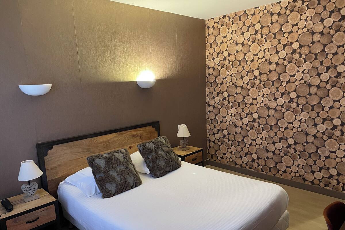 A neatly made bed with two pillows, a nightstand with a lamp, and a wall with a log pattern.