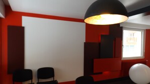 Una habitación moderna con una lámpara de techo negra, paredes rojas y una pizarra. Hay tres sillas negras y una mesa negra.