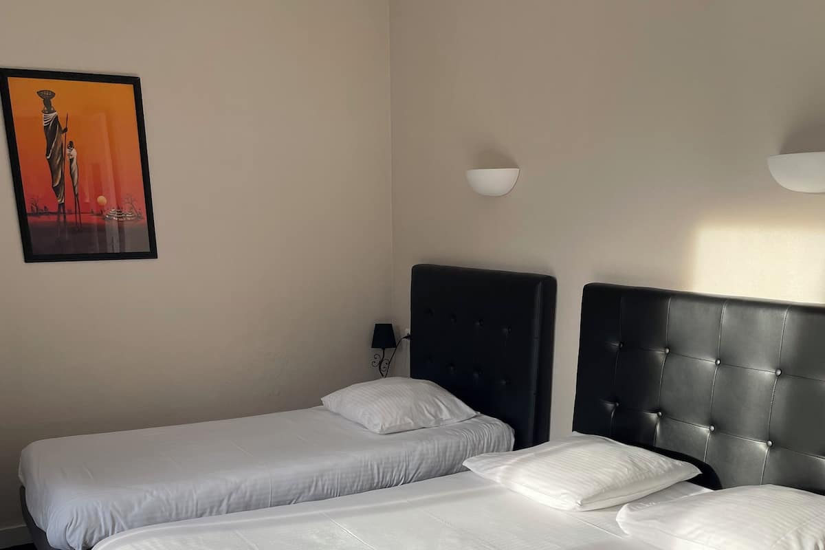 A hotel room with two beds, a painting on the wall, and a lamp.