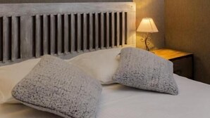 Habitación de hotel con diseño moderno, que incluye una cama grande con cabecera gris, dos almohadas grises, una mesita de noche con lámpara y una lámpara de pared.