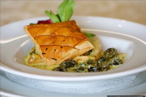 Un plato con un pastel dorado, acompañado de verduras y una flor rosa.